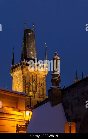 Beleuchteter Brückenturm der Kleinstadt und Statue, die abends in Prag im Schnee bedeckt ist Stockfoto