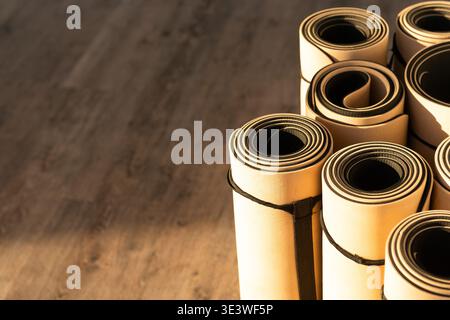 Eine Sammlung von gerollten Yogamatten, die ordentlich auf einem Holzboden gestapelt sind und sich im warmen Sonnenlicht sonnen. Perfekt für Fitnessbegeisterte oder Yogalehrer in Stockfoto
