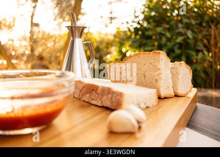 Frisch gebackenes rustikales Brot, serviert mit reichhaltigem Olivenöl, Reifen Tomaten und aromatischem Knoblauch auf einem Holzbrett. Perfekte Darstellung der mediterranen fla Stockfoto