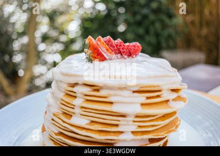 Ein köstlicher Stapel Pfannkuchen wird mit frischen, geschnittenen Erdbeeren belegt und mit cremiger weißer Schokoladensoße getränkt, was ein perfektes Frühstück schafft Stockfoto