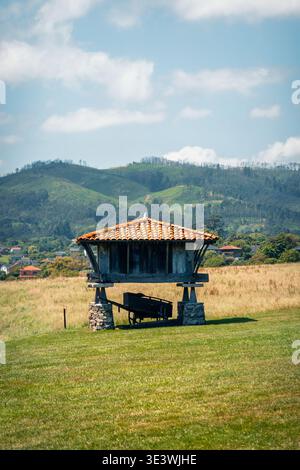Ein traditionelles horreo steht in der malerischen Landschaft von Cadavedo, Asturien, mit üppigen grünen Hügeln und einem leuchtend blauen Himmel im Hintergrund, zum Beispiel Stockfoto