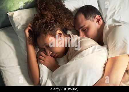 Junge Erwachsene Schwarze Frau und junger Erwachsener kaukasischer Mann schlafen zusammen im Bett, liegen nahe mit geschlossenen Augen, zeigen intime Momente eines Paares, das friedlich im Morgenlicht ruht Stockfoto