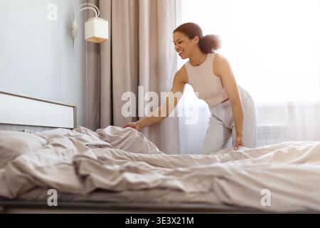 Lächelnde schwarze Frau, die morgens Bett macht, Decke und Kissen arrangiert Stockfoto