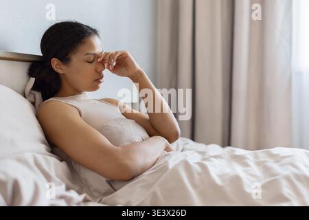 Junge schwarze Frau, die mit geschlossenen Augen im Bett liegt und den Nasensteg berührt Stockfoto