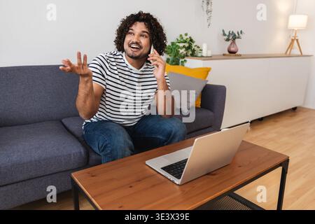 Junger indischer Mann lächelt, während er zu Hause mit dem Laptop fährt Stockfoto