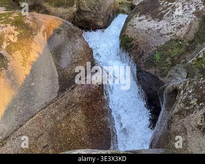 Rauschendes Wasser kaskadiert über moosbedeckte Felsen in einem lebendigen natürlichen Quellkonzept Stockfoto