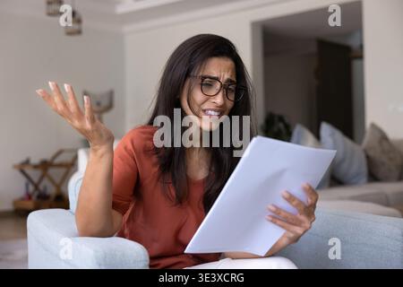 Junge frustrierte Frau, die zu Hause Dokumente liest Stockfoto