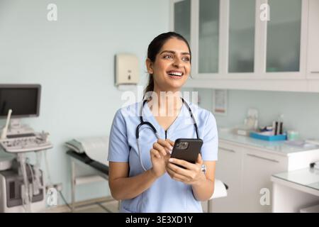 Lächelnde indische Krankenschwester, die ihr Smartphone benutzt Stockfoto