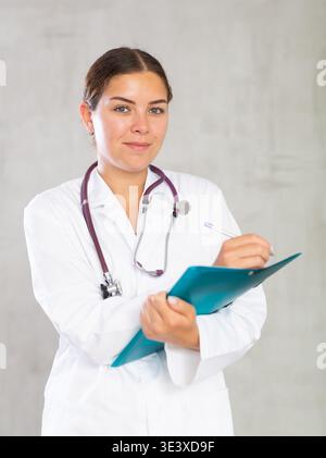 Eine Ärztin macht sich Notizen in Dokumenten, die eine Papiermappe in der Hand haben Stockfoto