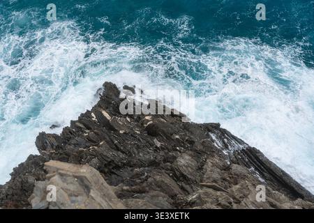 Mächtige Meereswellen krachen gegen dunkle felsige Ufer. Natürliche Meereslandschaft, Meeresenergie und dramatische Küstenlandschaft Stockfoto