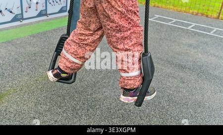 Kinderfüße auf einer Outdoor-Fitnessschaukel auf einem Spielplatz erfassen aktive Kindheit, Erholung, Bewegung und gesunden Lebensstil in einem urbanen Park. Stockfoto