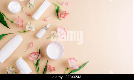 Hautpflegeprodukte mit Alstroemerieblumen auf beigem Hintergrund. Minimale Schönheitskomposition mit Kosmetikbehältern. Draufsicht, flach, Kopierbereich. Stockfoto