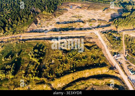 Weitläufige Sandsteinbrüche, von oben gesehen. Ein Feldweg schlängelt sich durch das Industriegebiet, im Kontrast zu den nahe gelegenen, üppig grünen Wäldern unter einem Stockfoto