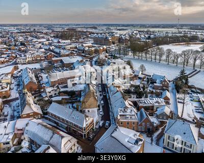 Aus der Vogelperspektive auf eine verschneite europäische Stadtstraße mit traditionellen Backsteinhäusern. Eine malerische Winterstadt mit mattierten Dächern, geparkten Autos und Stockfoto