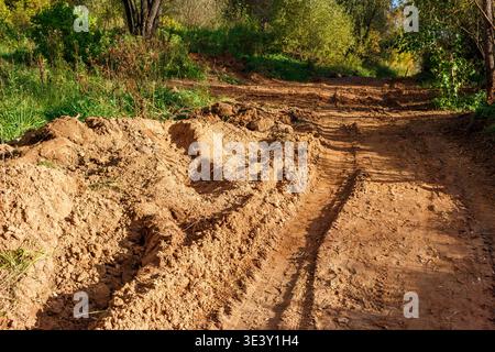 Tiefe Reifenspuren führen durch eine raue, schlammige Feldstraße und schlängeln sich in eine sonnenverwöhnte ländliche Landschaft mit üppigem Grün Stockfoto