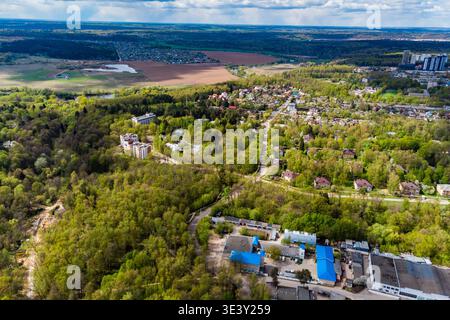 Die weitläufigen Vorstädte liegen inmitten von grünen Frühlingswäldern, die von oben erfasst werden. Ein Flickenteppich aus Häusern, Straßen und aufkeimender Entwicklung unter freiem Himmel Stockfoto