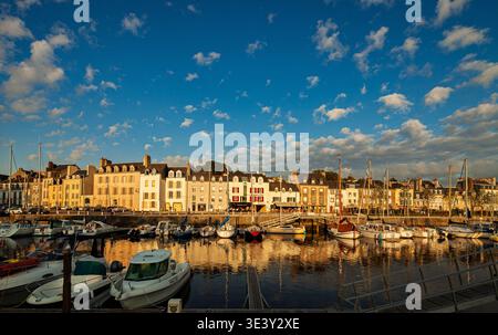 Vannes' Bernard Moitessier Dock in warmem goldenem Licht getaucht. Historische Gebäude säumen die Uferpromenade und spiegeln sich wunderschön im ruhigen Yachthafen Wasser u wider Stockfoto