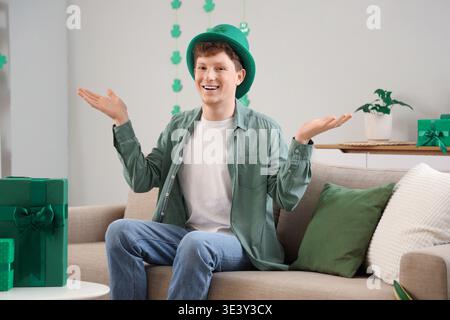Rothaariger junger Mann mit Kobold-Hut sitzt zu Hause am St. Patrick's Day Stockfoto