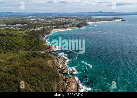 Drohnenblick auf eine felsige Küste, die in Richtung Burgess Beach und One Mile Beach in Forster führt. Die Perspektive fängt zerklüftete Küstenformationen ein Stockfoto
