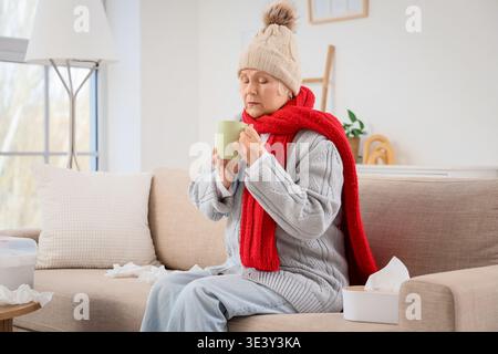 Kranke ältere Frau mit einer Tasse Tee, die zu Hause auf dem Sofa sitzt Stockfoto