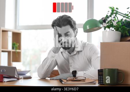 Müder männlicher Büroangestellter sitzt am Tisch. Burnout-Konzept Stockfoto