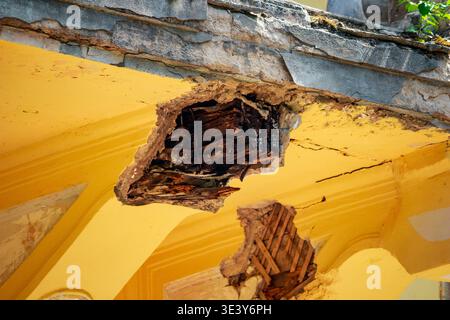 Zerbröckelnder alter Balkon mit freiliegenden Holzstützen und gerissenem gelbem Putz. Struktureller Zerfall und Vernachlässigung offensichtlich, was auf dringende Reparaturbedürfnisse hindeutet Stockfoto