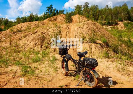 Ein elektrisches Fatbike liegt auf einem zerklüfteten Sandweg und ist bereit für abenteuerliche Offroad-Entdeckungen. Eine Reise in die wilde Natur unter einem hellen Sommerhimmel: Stockfoto
