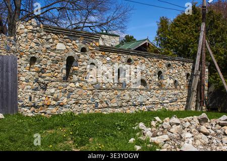 Farbenfrohe Steinmauer, handwerkliches Mauerwerk mit einzigartigen Bogennischen, steht vor einem hellblauen Himmel, umgeben von leuchtendem grünem Frühlingsgras Stockfoto