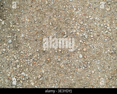 Körnige Erdstruktur mit gemischten Kieseln und Sand. Natürliche Töne deuten auf eine Umgebung im Freien oder im Bauwesen hin. Geeignet für Architektur, Design oder Stockfoto