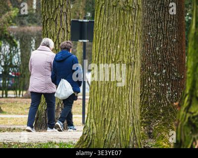 Altes Paar spaziert durch den Herbstpark. Bäume stehen hoch, Blätter verstreut. Sie schlendern in der Nähe und teilen ruhige Momente. Weiches Sonnenlicht filtert durch Kleie Stockfoto