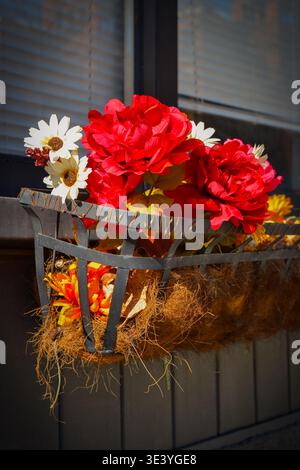 Easton, Pennsylvania, USA – 9. Februar 2026: Vertikale Nahaufnahme künstlicher Herbstblumen in einem schwarzen Metallfenster. Stockfoto