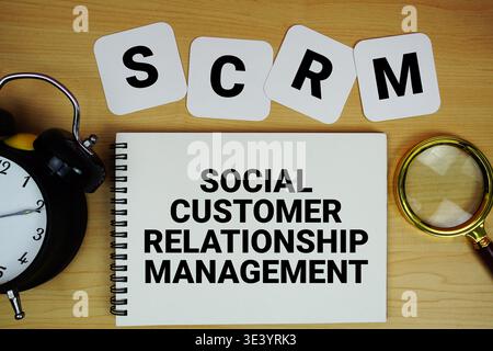 SCRM Social Customer Relationship Management-Text auf Notizblock mit Lupe und Wecker auf hölzernem Hintergrund Stockfoto
