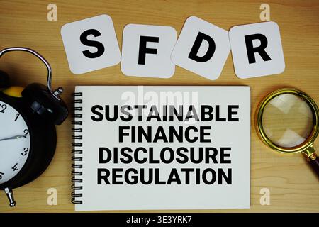 Text der SFDR-Verordnung zur Offenlegung nachhaltiger Finanzen auf Notizblock mit Lupe und Wecker auf hölzernem Hintergrund Stockfoto