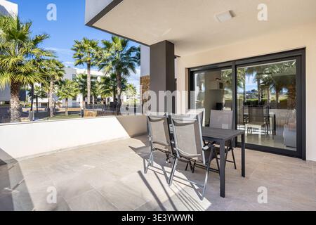 Stilvolle Apartmentterrasse mit Gartenmöbeln, schattigem Terrassenbereich und großen Glastüren in einem modernen Wohnbereich Stockfoto
