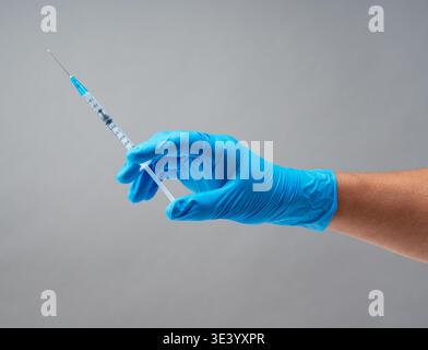 Hand in blauem medizinischen Handschuh mit steriler Spritze mit Nadel vor grauem Hintergrund Stockfoto