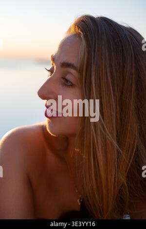 Porträt der Frau bei Sonnenuntergang mit einer lächelnden jungen Frau am Strand während der goldenen Stunde, die einen ruhigen und friedlichen Sommerabend genießt Stockfoto