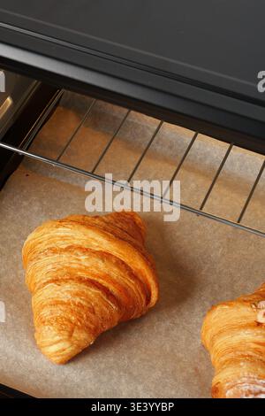 Frisch gebackene Croissants auf einem Backblech im Backofen zum Kochen in einer Bäckerei Stockfoto