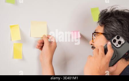 Geschäftsmann, der während der Planung eines neuen Projekts telefoniert, mit Haftnotizen im Büro. Seitenansicht, selektiver Fokus. Organisationskonzept. Stockfoto