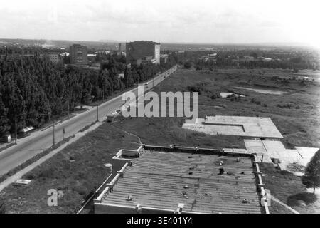 Sloviansk, Mitte der 1990er Jahre, Artem Microdistrikt (Bäckerei-Bereich). Ein historisches Schwarzweiß-Foto, das eine ruhige Hochwinkelperspektive über eine integrierte Industrie- und Wohnzone zeigt. Die geometrische, mehrstöckige Fassade der örtlichen Bäckerei steht im Zentrum. Ein leerer gepflasterter Innenhof liegt auf der linken Seite, während dichte grüne Bäume und hoch aufragende mehrstöckige Wohnhäuser die städtische Kulisse abrunden. Dieser detailreiche Schnappschuss aus dem Archiv zeigt das postsowjetische Stadtdesign und den friedlichen Donbass auf elegante Weise. Stockfoto