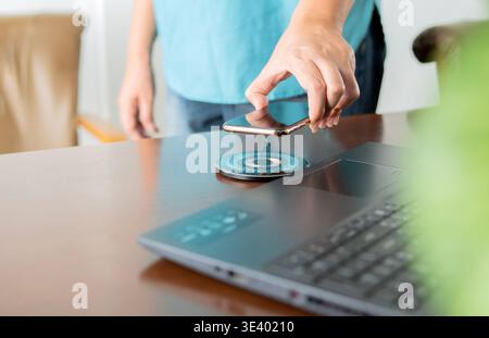 Handauflage des Mobiltelefons am Arbeitsplatz in ein kabelloses Akkuladegerät. Moderne Technologie, tragbares Schnellladegerät. Selektiver Fokus. Stockfoto