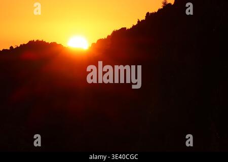 Einfache und ruhige Landschaft mit einem glühenden Sonnenuntergang, der hinter einer Bergsilhouette abfällt. Stockfoto