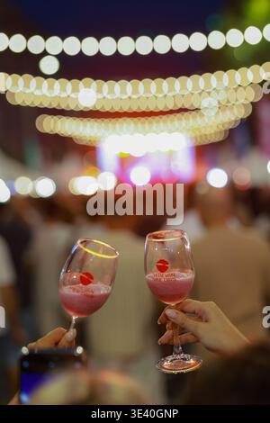 Das Jerewan Wine Days Festival wird durch zwei Gläser mit prickelndem Getränk vor Abendlichtern und einer verschwommenen Festivalmenge gezeigt. Stockfoto