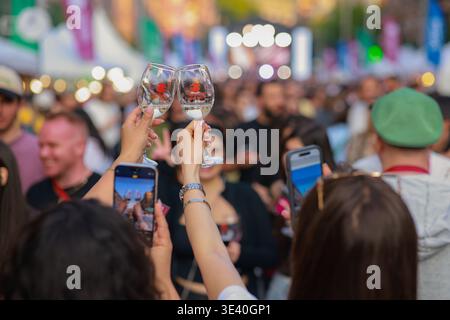 Das Festival der Jerewan Wine Days wird in einem lebhaften Moment der Menschenmenge festgehalten, während zwei Weißweingläser für ein Foto hochgezogen werden. Stockfoto