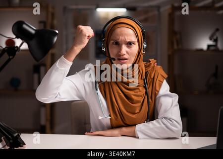 Weibliche muslimische Ärztin im Hijab oder Arzttherapeutin im weißen Mantel tragen Headset mit Mikrofon arbeiten mit Laptop schreiend und schreiend Wut und A Stockfoto