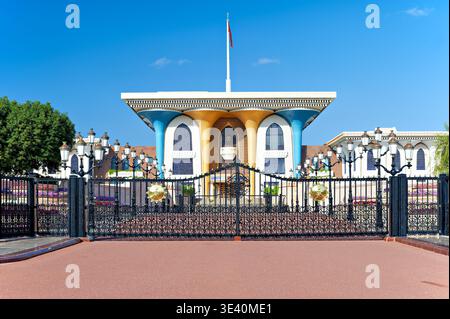 Al Alam Palace in Muscat zeigt seine einzigartige Architektur unter einem klaren blauen Himmel. Besucher bewundern das Gebäude und die Gärten in der Nähe. Stockfoto