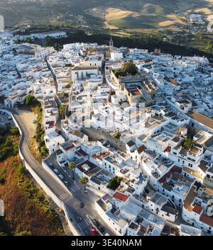 Aus der Vogelperspektive auf sonnengeküsste weiße Gebäude, die den Hügel hinunterragen, im Kontrast zum grünen Tal und den fernen Bergen, Vejer de la Frontera, Stockfoto