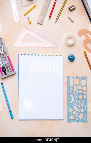 Leeres Notizbuch mit Werkzeugen zur Geometrieentwicklung im Hintergrund. Verschiedene Schreibwaren für Schule oder Ingenieurwesen Flat Lay. Kopierbereich mit Schreibtischblick. Stockfoto