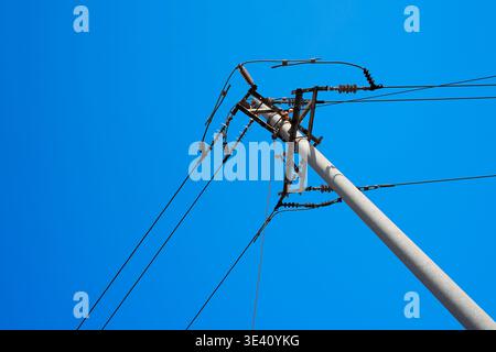 Nahaufnahme von Isolatoren für Außenleitungen und Hardware, die an einem Versorgungsmast montiert sind und elektrische Übertragungskomponenten gegen ein klares blaues s zeigen Stockfoto