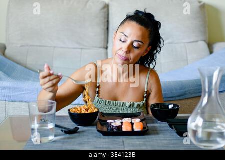 Zwanglose Frau, die Sushi allein zu Hause genießt. Eine entspannte Frau genießt hausgemachtes Sushi mit einem Lächeln Stockfoto