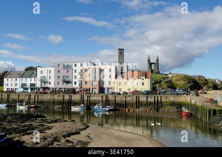 Der Hafen von St. Andrews vom Pier aus gesehen mit angelegten Fischerbooten, pastellfarbenen Häusern am Wasser und historischen Kathedralruinen auf dem Hügel unter einem hellen Blau Stockfoto